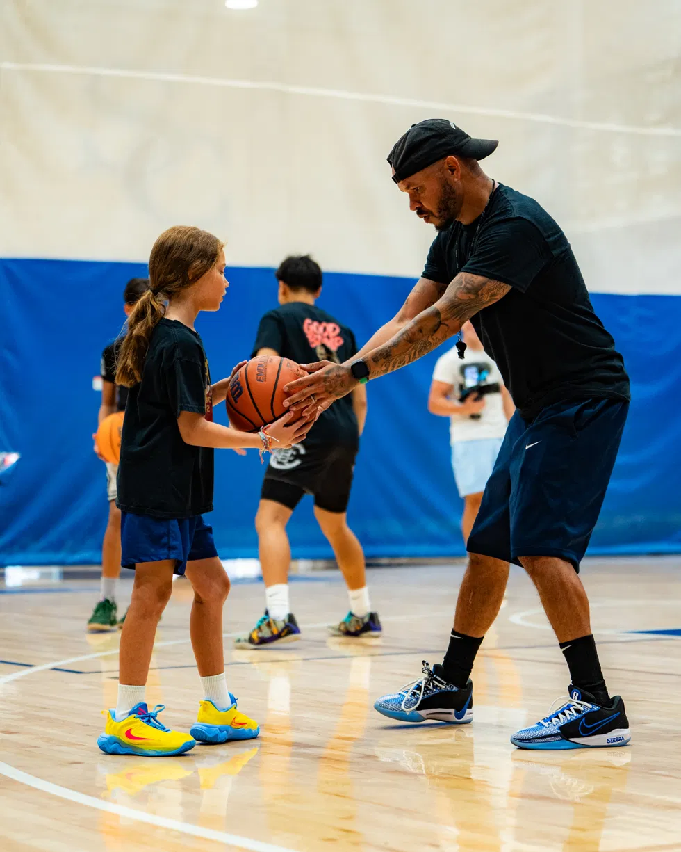 Coach Sandy handing a basketball to a young player during instruction