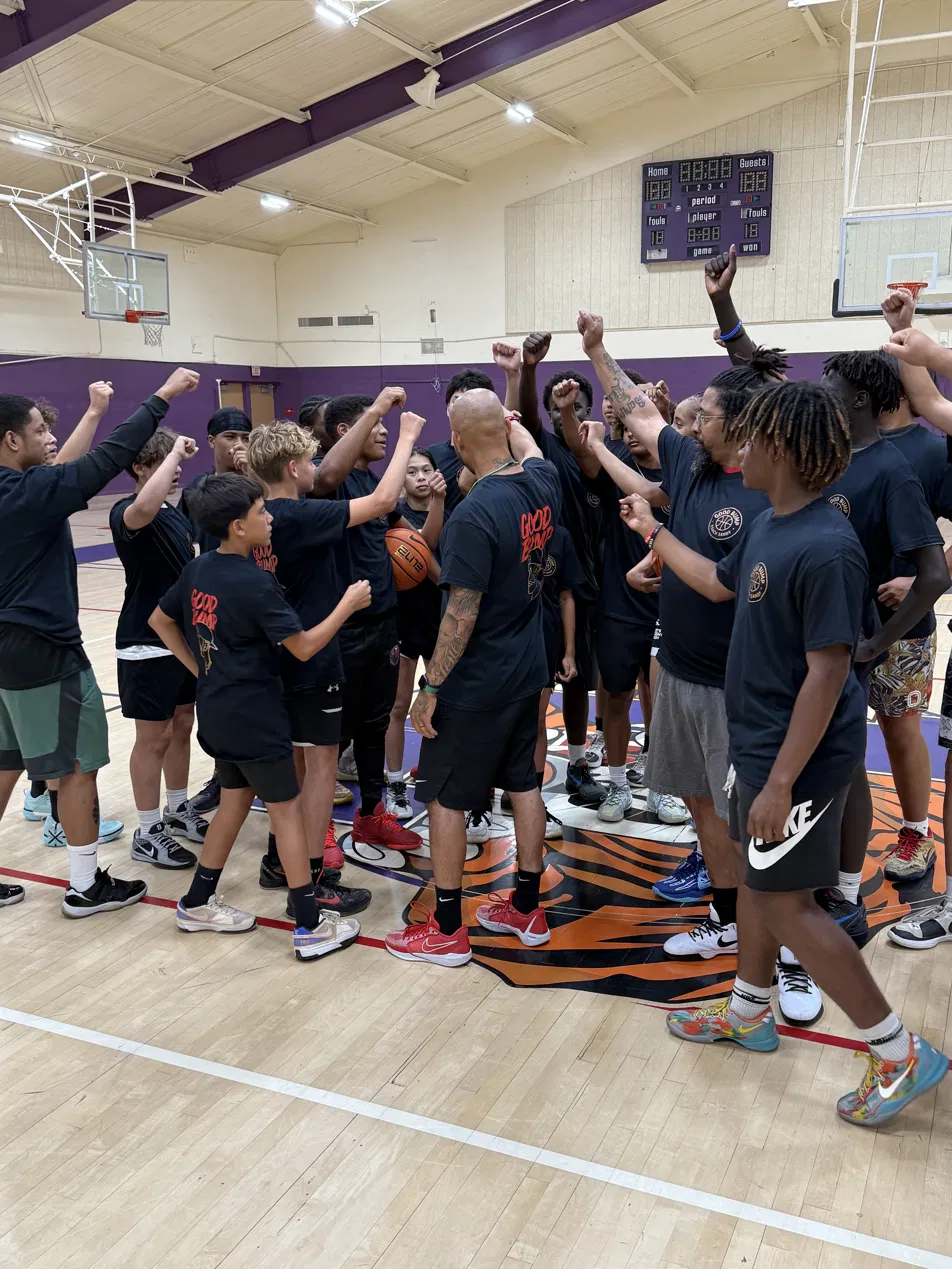 Players and Coach Sandy in a team huddle with fists raised in the gym