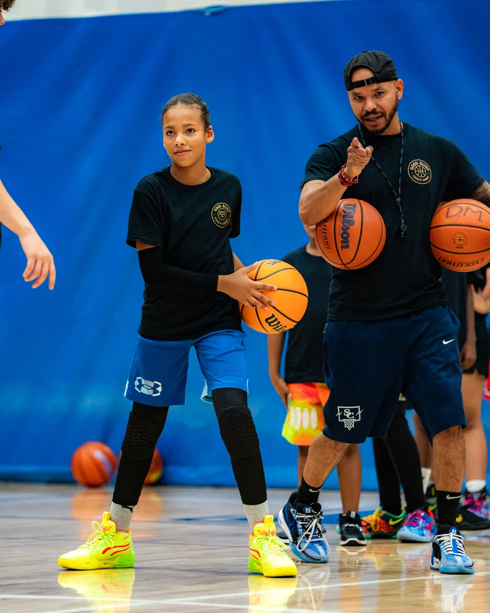 Coach Sandy coaching a young player holding a basketball on the court
