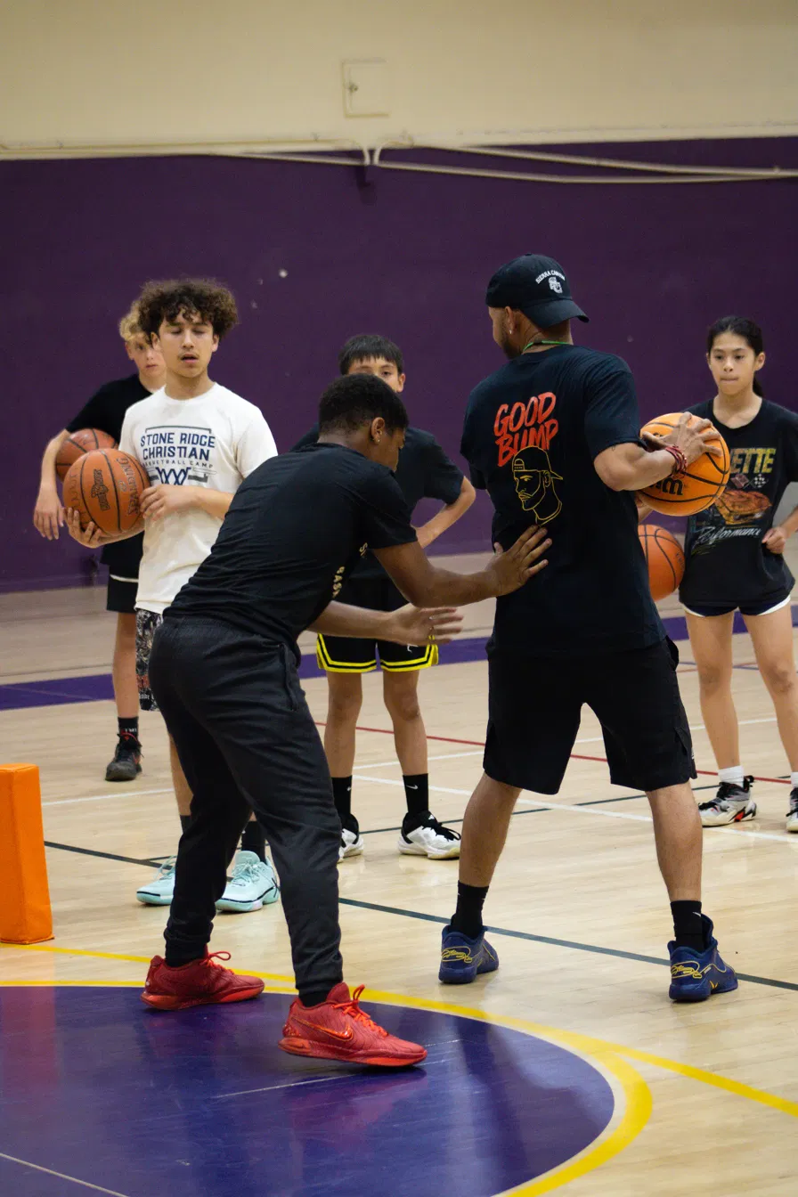 Coach Sandy teaching ball handling with players gathered around him